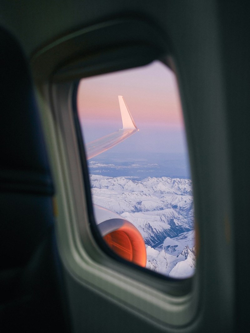 The view from inside of a flying airplane showing snowy mountain tops.