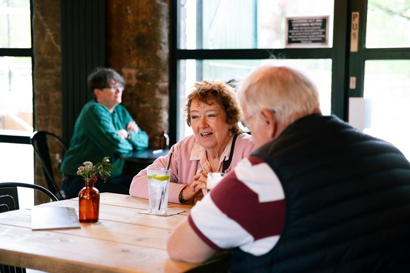 An older woman sits at a table with a companion