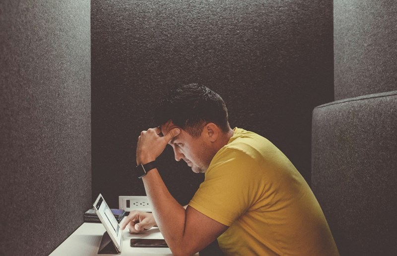 A man hunches over his computer at a table