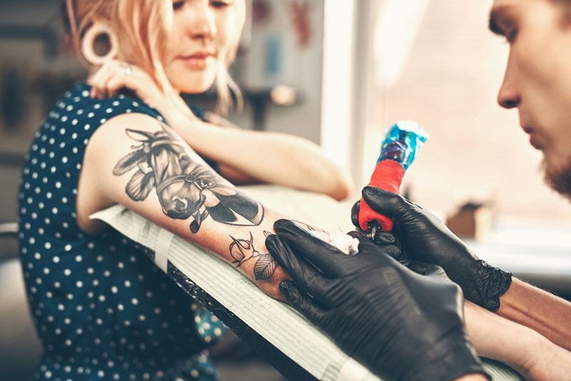 A tattoo artist gives a young woman a tattoo