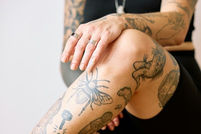 A woman covered in tattoos sits with her arms crossed