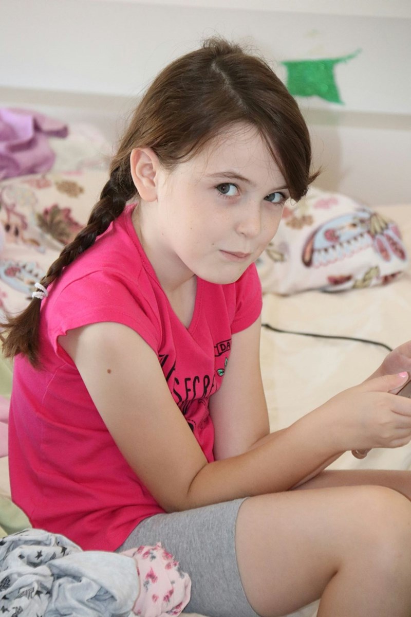 Girl in pink t-shirt sitting on bed