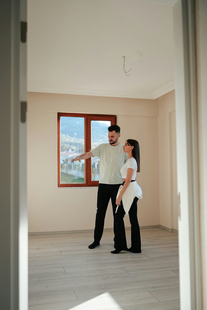 Man and a woman standing in an apartment looking at a wall.