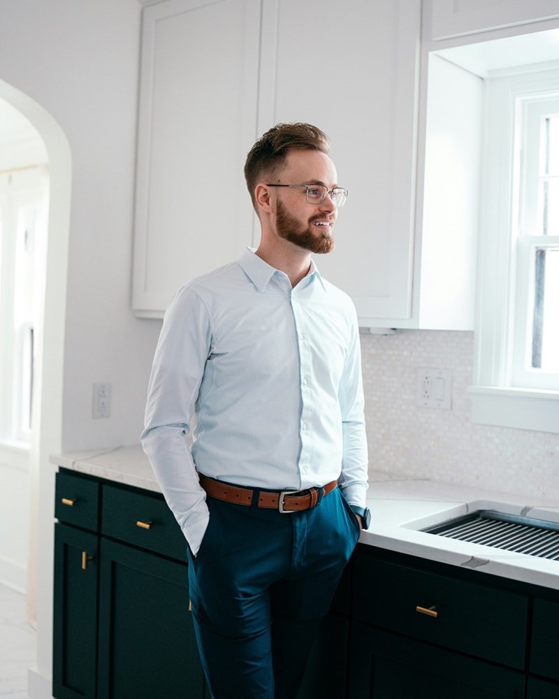 Man with a beard wearing a suit standing up in a kitchen.