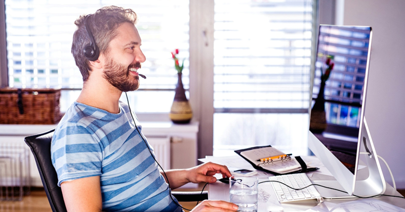 A man working from home while wearing a headset looks at his computer