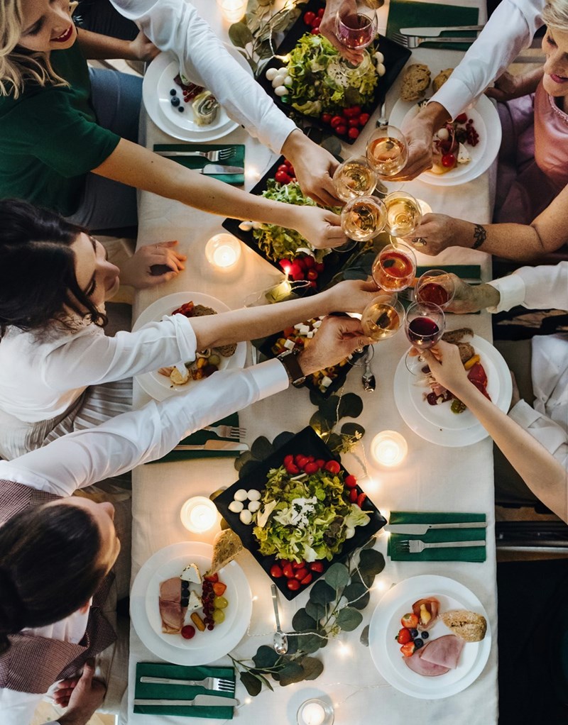 A midsection of a big family sitting at a table at an indoor birthday party clinking glasses a top view