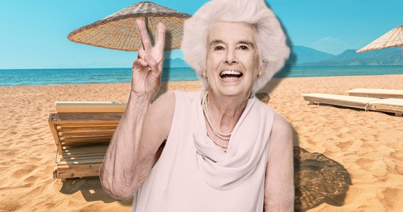 Older woman makes a peace sign while at a beautiful beach with turquoise waters.