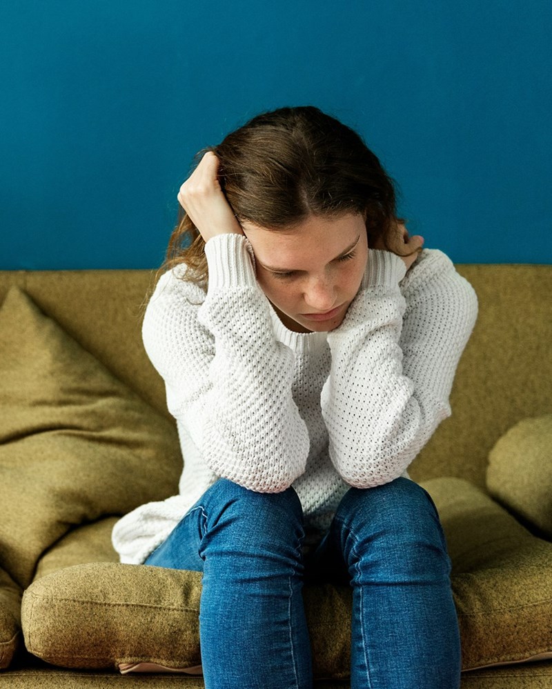 Stressed teenage girl sitting on a yellow couch with her hands in her head.