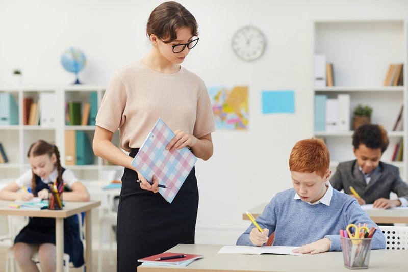 A young teacher looks over a student's shoulder to check his work.