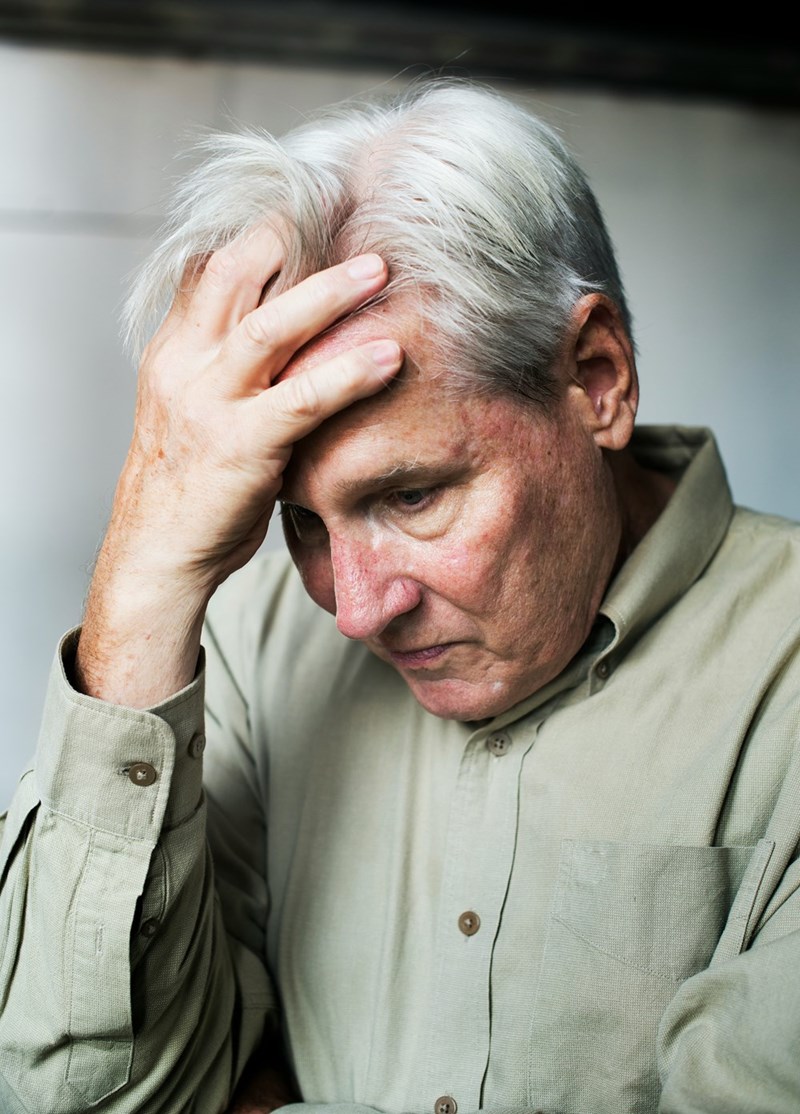 An older man looks upset as he puts his head in his hand.