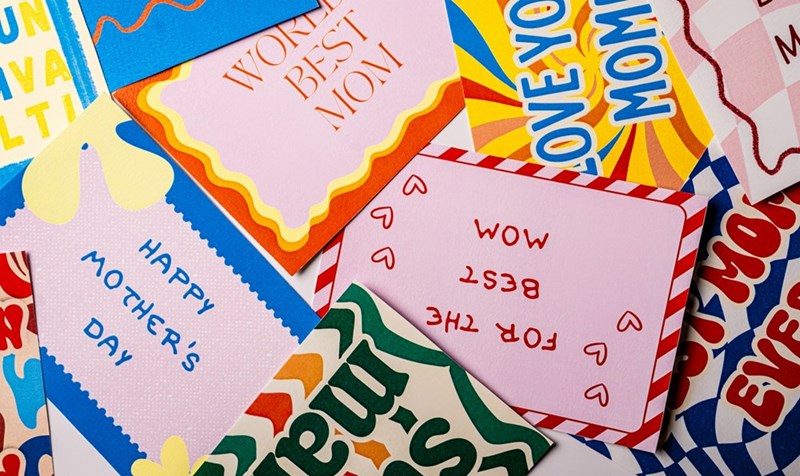 A bright collection of colorful Mother’s Day cards and decorative designs spread across a table with playful retro-inspired typography and patterns.