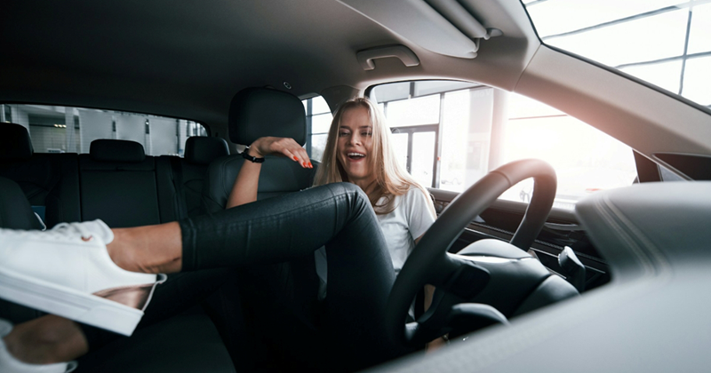 A young woman laughs as she sits sideways in the driver's seat of a car
