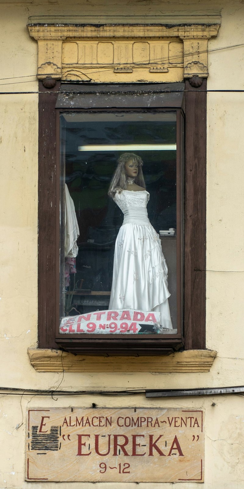 A window of a shop with a mannequin wearing a white wedding dress.