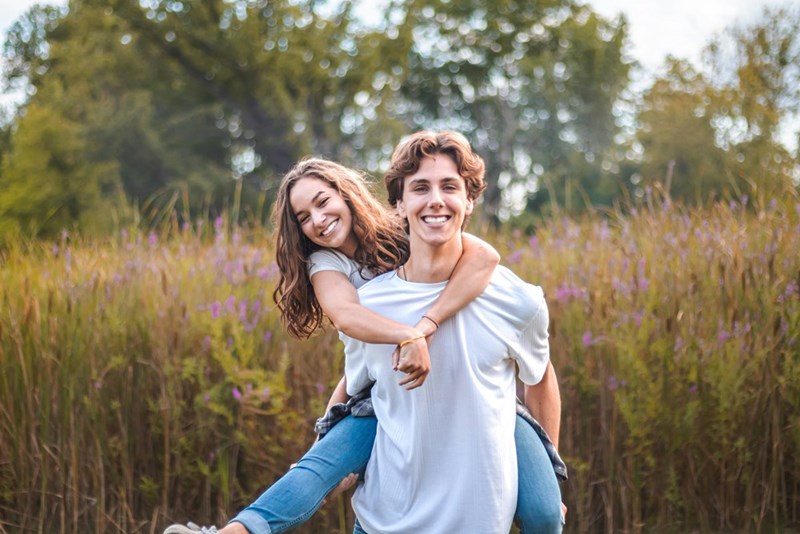 Woman smiling hanging on the back of a man both smiling in a lavender field.