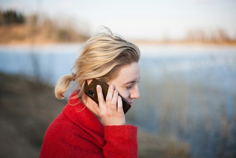 Woman wearing a red coat holding a cellphone while looking to the river.