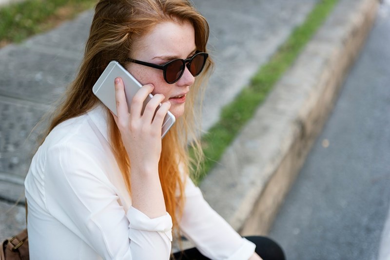 Woman sitting on a bench wearing sunglasses talking over the cellphone.