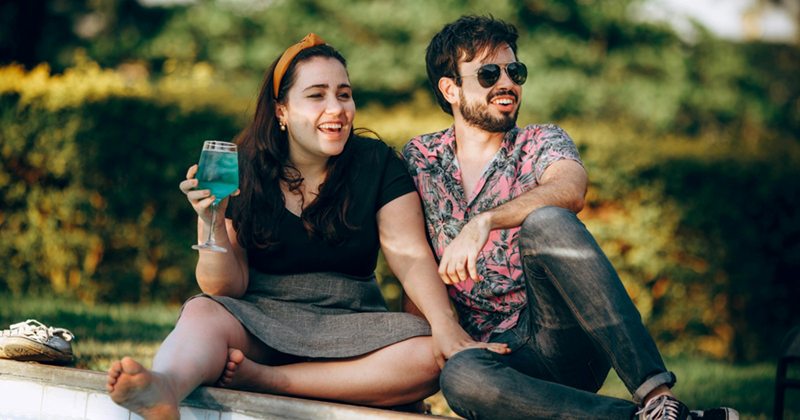 A woman holding a blue drink and a man sit next to one another outside