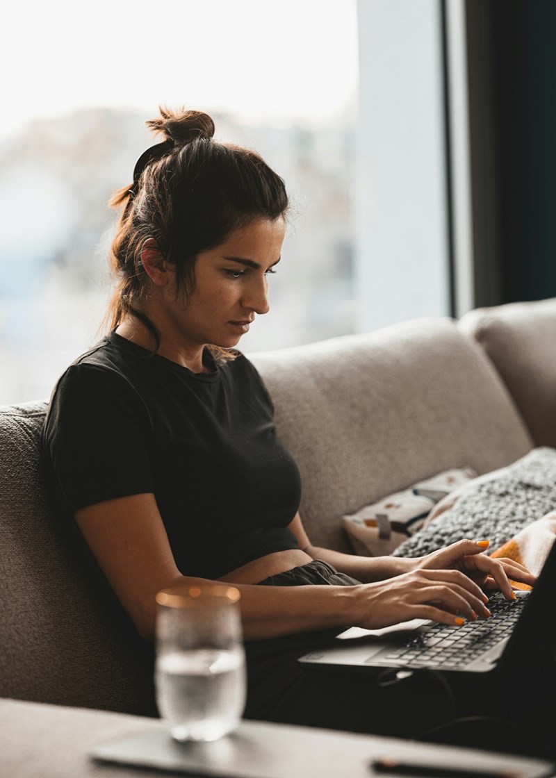 Woman working on laptop, typing while sitting on a couch