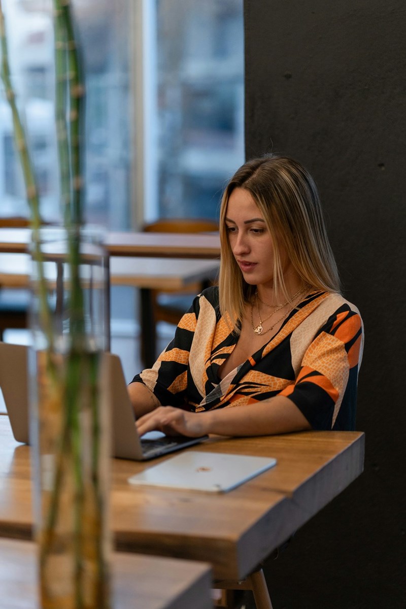 Woman using a laptop at a café table in a modern workspace with warm lighting and contemporary decor.