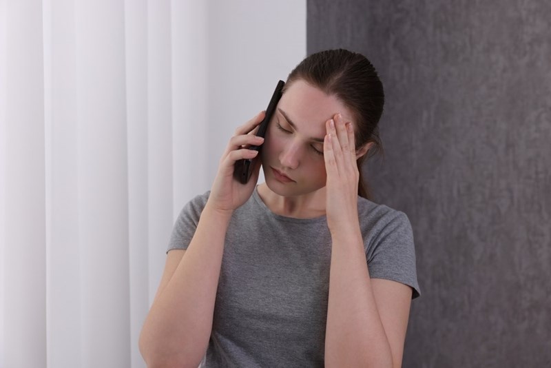 Woman talking on a smartphone with her hand on her forehead, appearing stressed indoors.