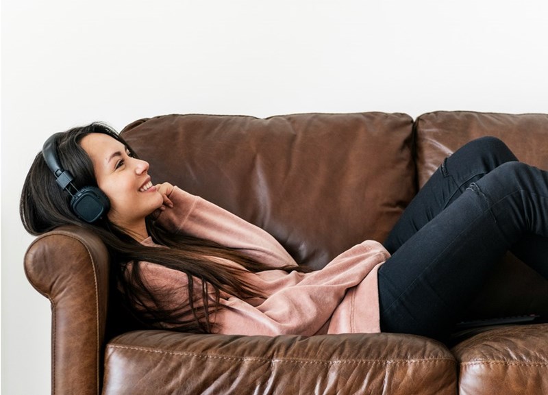 Woman relaxing on a leather couch wearing headphones and smiling while listening indoors.