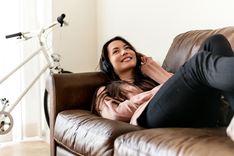 Woman lying on a leather couch wearing headphones with a bicycle visible in the background.