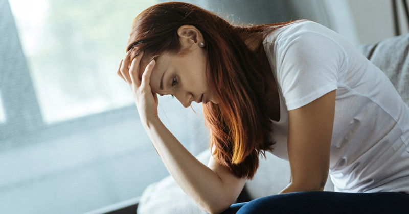 A woman holds her head in her hand while sitting on the couch