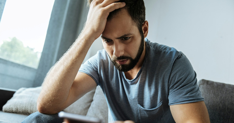 A man touches his hair with his hand while sitting on a couch