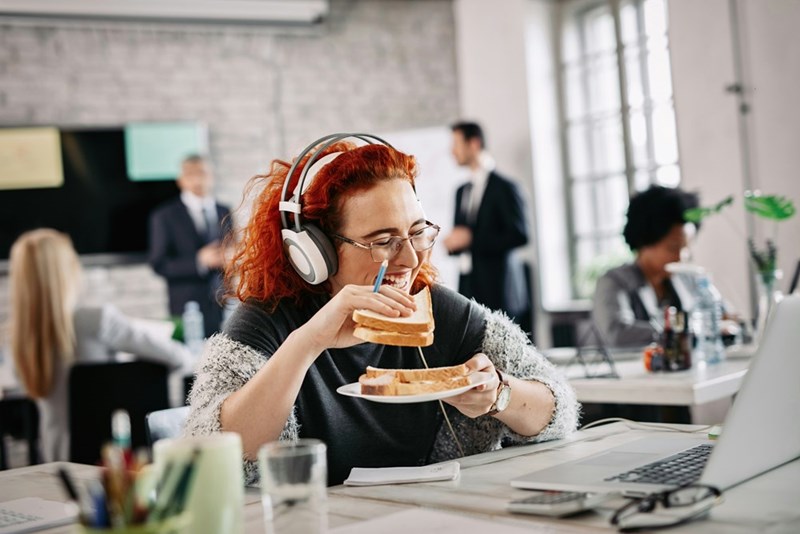 A businesswoman eats a sandwich at her desk