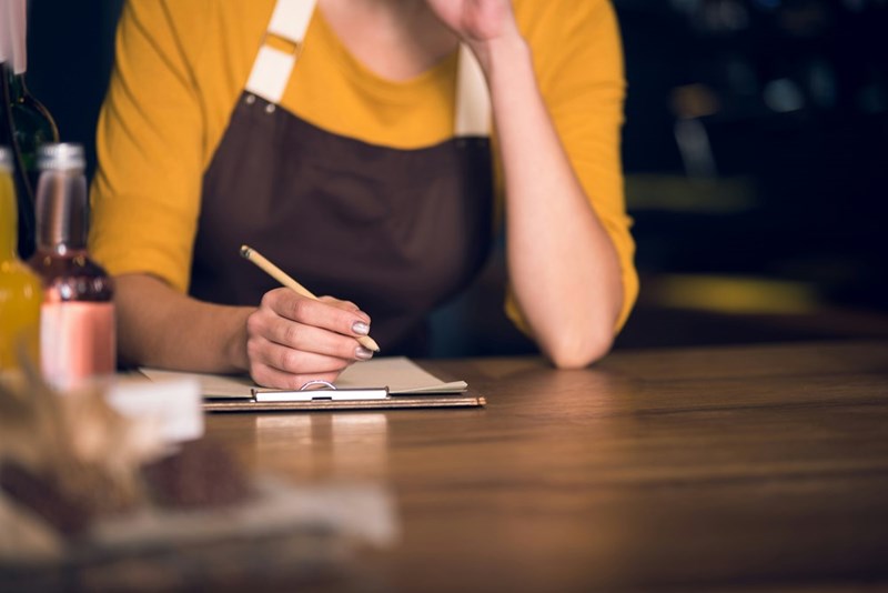 Female hand writing on a paper at work wearing an apron.