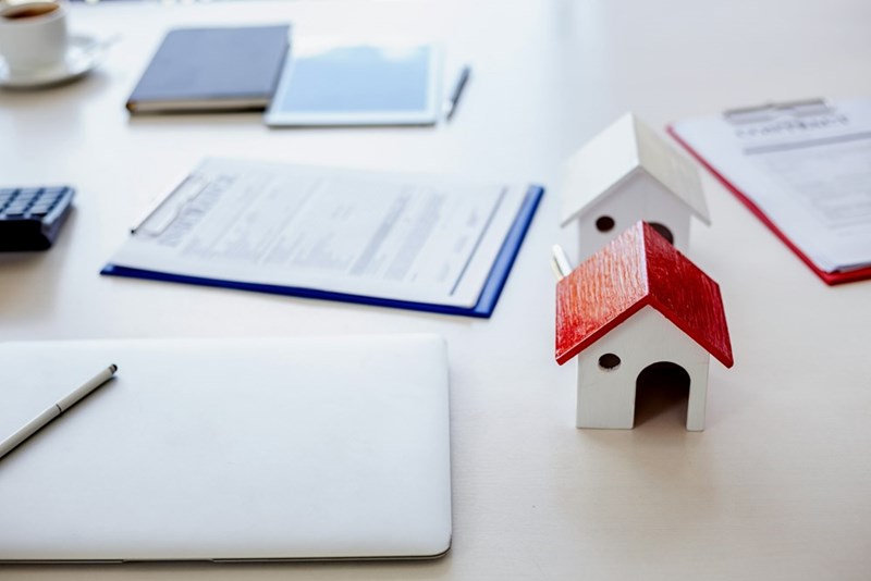 Rental paperwork and a small model house sit on a desk, symbolizing rising housing costs and landlord-tenant disputes.