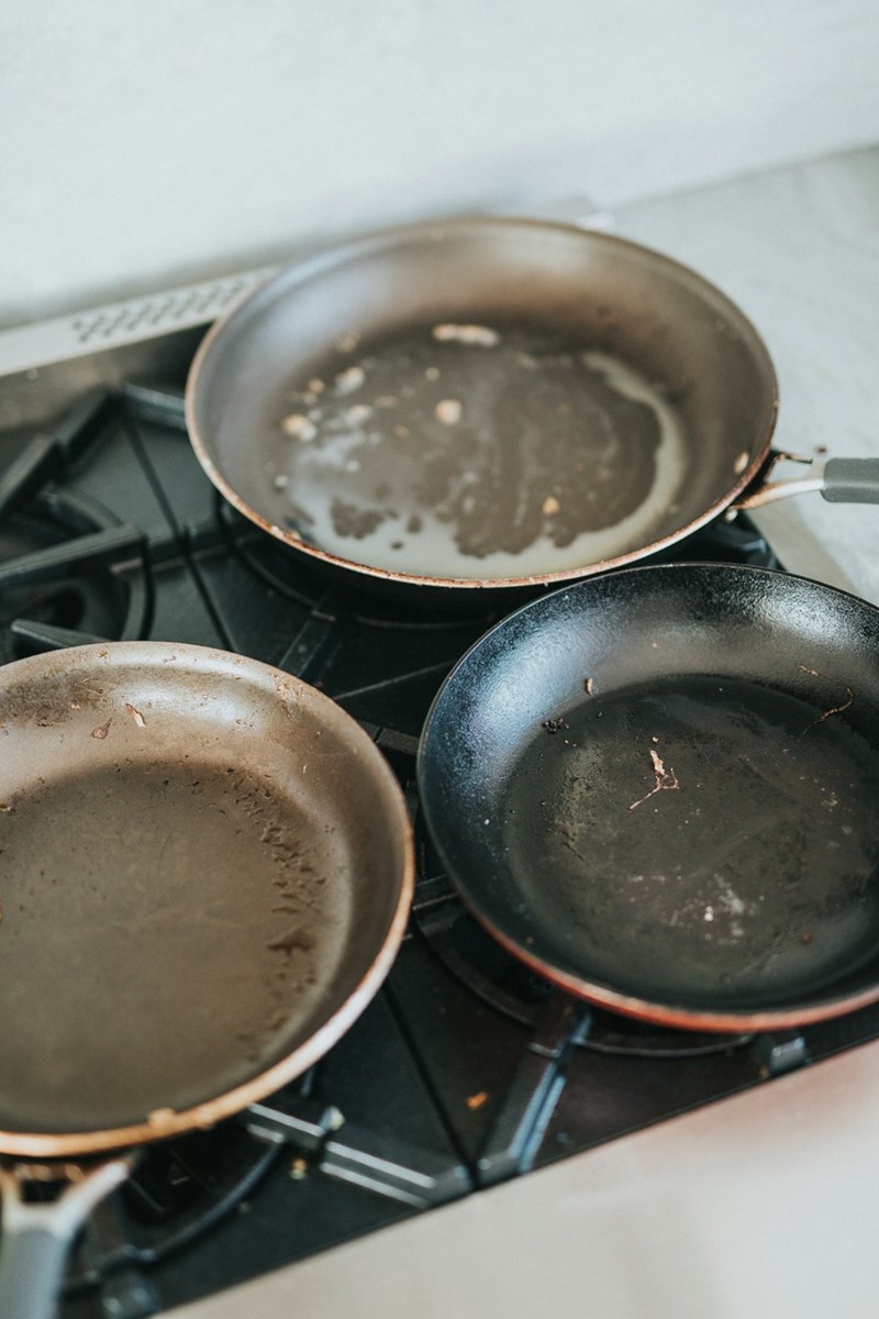 Dirty frying pans left on a stovetop after cooking multiple meals in a busy family kitchen.