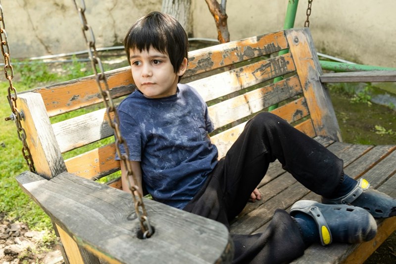 A young boy sitting on a wooden swing