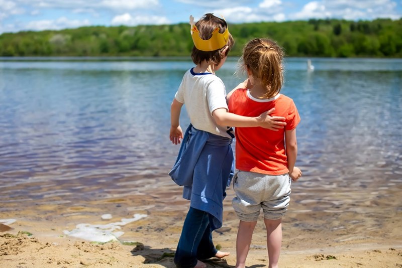 Young brother and sister relax outside in the summer weather by a large lake.