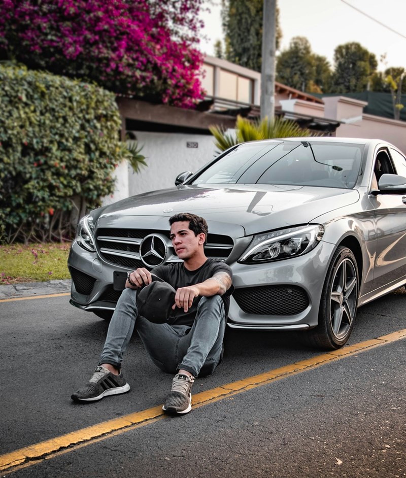 Man sitting beside silver Mercedes Benz car outdoors