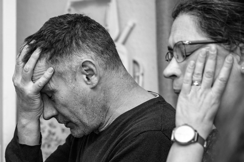 stressed couple sitting indoors with hands on their faces in a black-and-white photo.