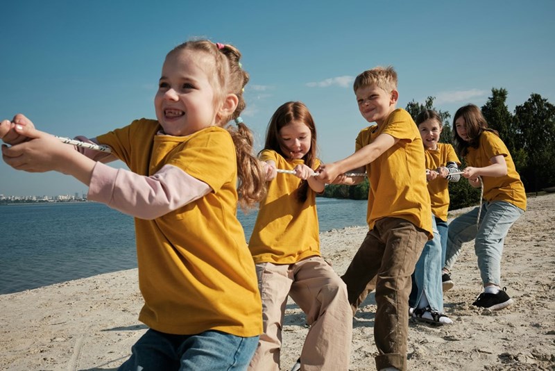 Group of kids attending summer camp play tug-of-war with a rope.