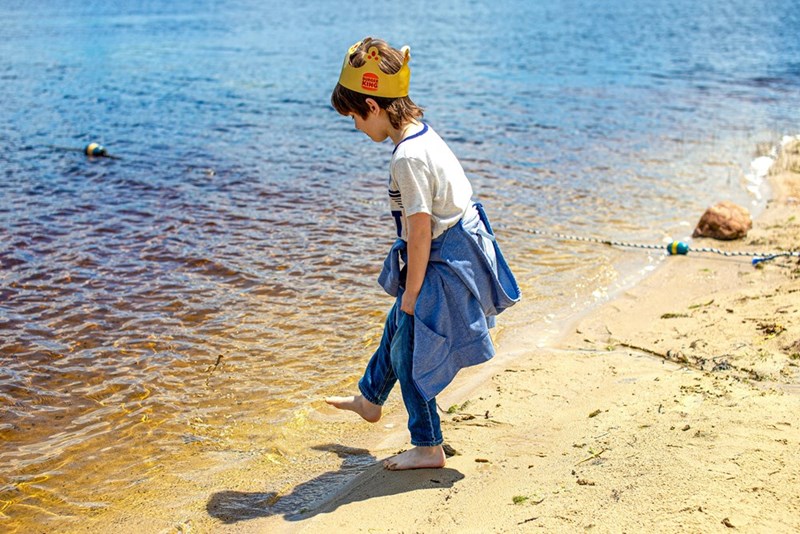 Little boy dips his toes in the water at a lake.