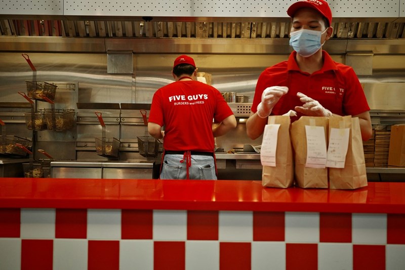 A fast food employee wearing a mask prepared food orders in the kitchen.