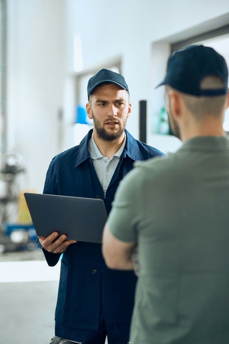 A technician speaks to his manager, who holds a laptop in his hands.