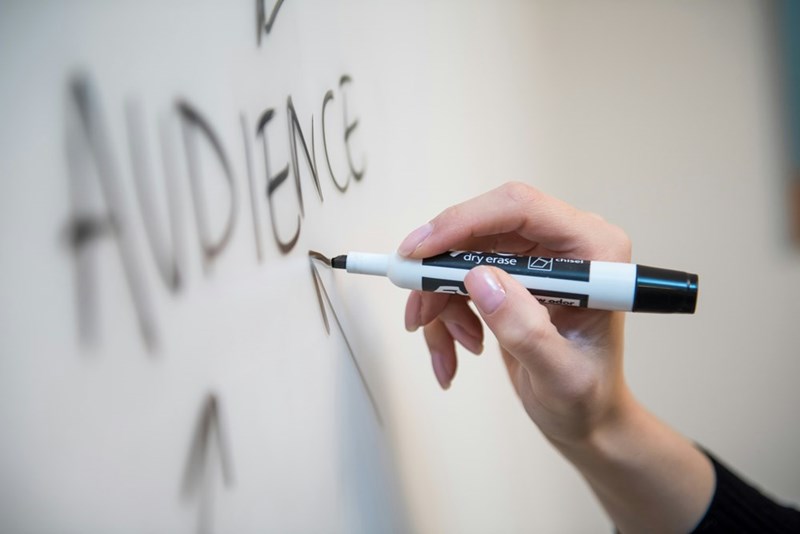 A person draws the word audience on a whiteboard