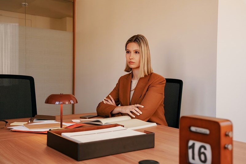 A female employee sits at her desk in the office with crossed arms.