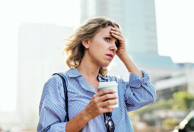 Upset woman walking outside with a cup of coffee holding her head.