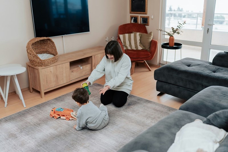 A wide shot of a woman playing games with her nephew while babysitting in her apartment.