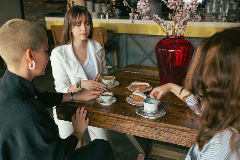 Woman staring at a blank point in a table coffee shop surrounded by friends.