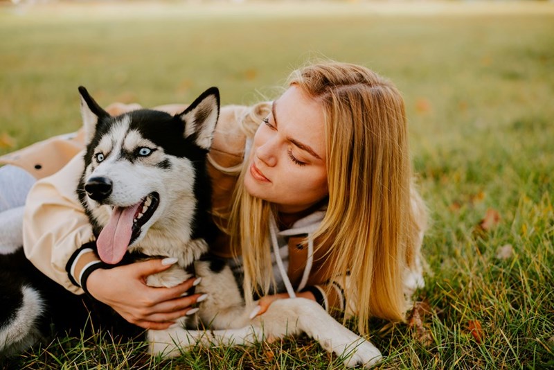 A woman laying on the grass with a husky dog