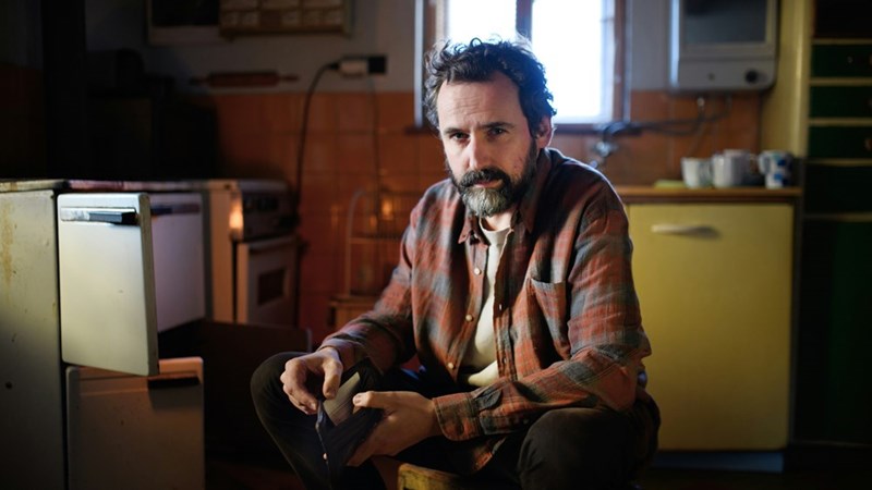 Worried man sitting in a small kitchen while checking a wallet
