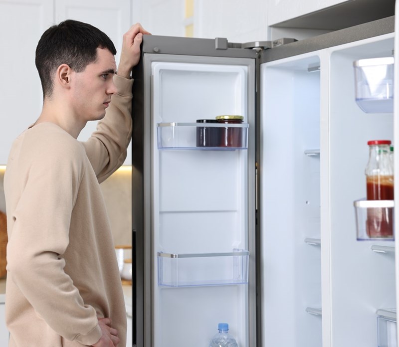 Man looking into an almost empty refrigerator while standing in a modern kitchen at home.
