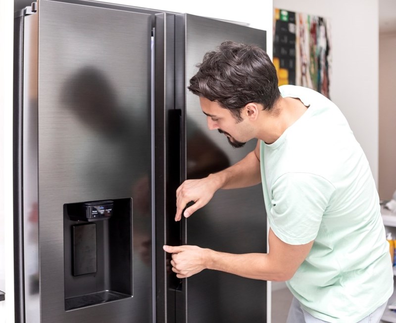 Man opening a large stainless steel refrigerator while checking inside in a modern kitchen.