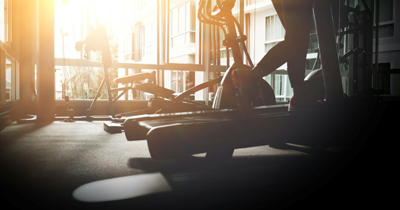 A woman's legs running on a treadmill in a gym as the sunrise shines through the window